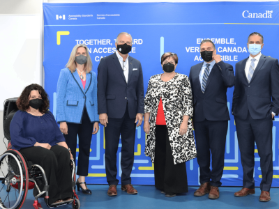 Six individuals with face masks are in front of a blue backdrop. They represent two organizations: Accessibility Standards Canada and the International Code Council.