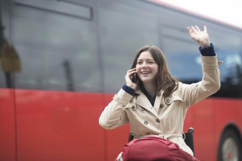 Young woman using wheelchair waving from city bus station